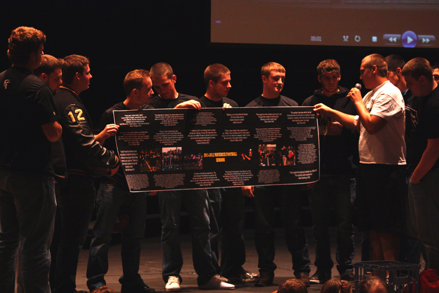 Senior football players present a banner of all of their quotes and seven pictures from this past season as a surprise to their coaches. Many of the players passed the microphone and got down on one knee to read what they had written to their shocked coaches. Photo by A. Esser