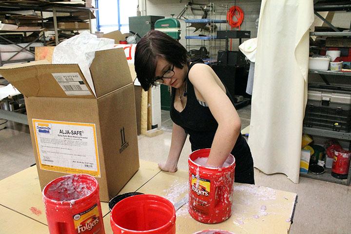 Angelina Wiglesworth, junior, places her hand in a bucket of plaster in Portfolio Development. The plaster will make a mold of her hand when dry.