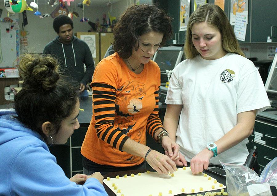 Robbi Herrington, sciences, assists students Courtney Sellens and Lauryn Chavez, both 12, during AP Bio.  They were working on making cell membranes from macaroni noodles. Photo by B. Jones-Rupp