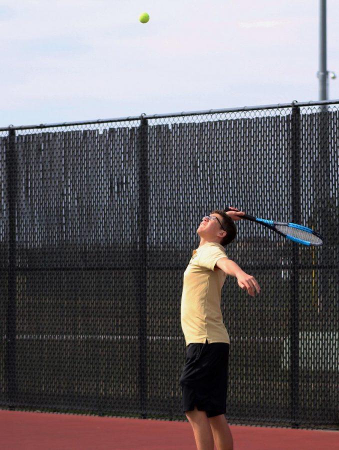 Freshman Karsten Shields strenuously serves the ball during their first tennis duel against Maize High on the last Thursday before Spring Break. Temperatures were around 60 degrees, and wind during the match caused difficulties during serves between the teams.