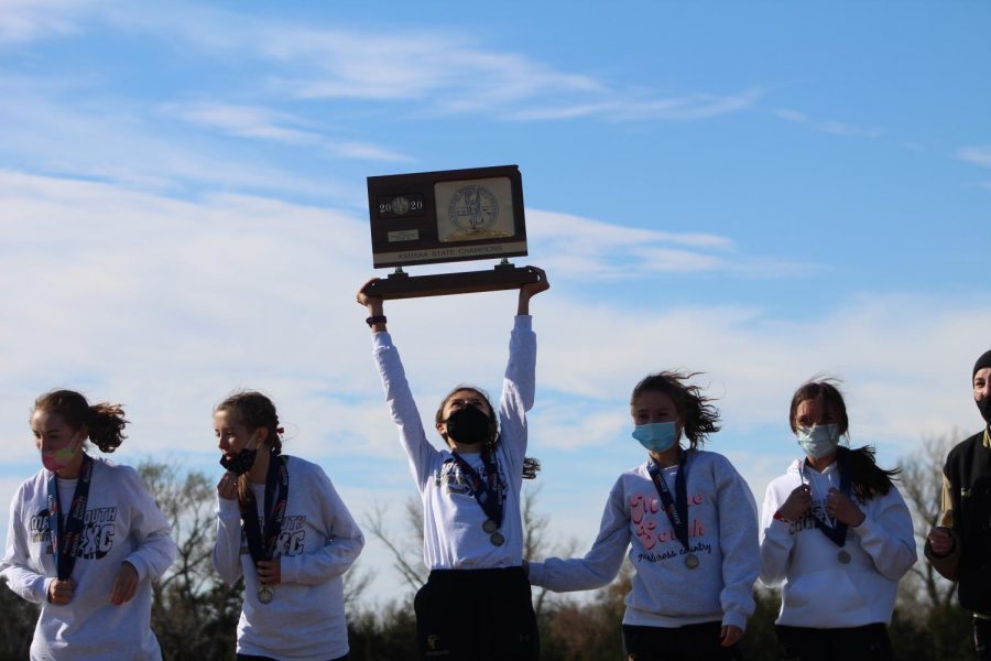 After winning the KSHAA State Championship last Saturday, the girls cross country team holds up their trophy for the hundreds of spectators in Augusta. The girls won by one point against Bishop Carroll on the day with 58 points total. 