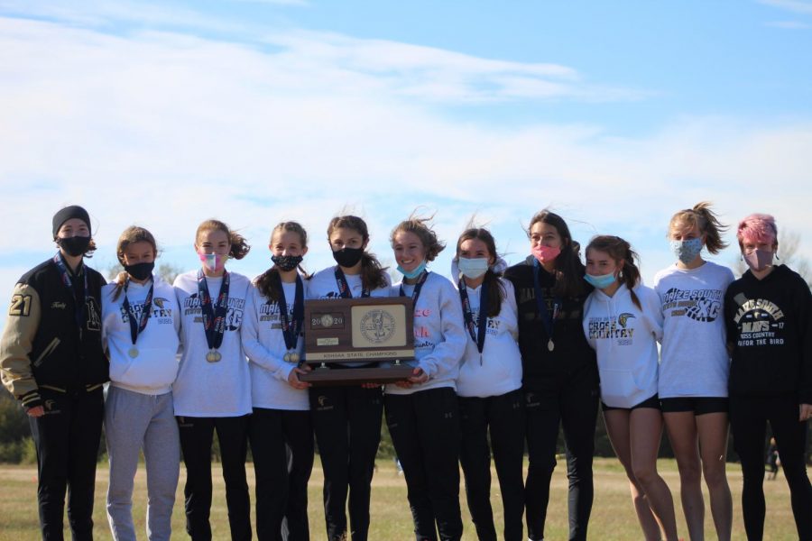Proudly holding their 5A state trophy, the girls on the Maize South cross country team smile under their masks on stage to receive praise for their win.  Amber Eichkorn, the Maize South cross country coach, celebrated the victory with the team on stage as they accepted the award.  