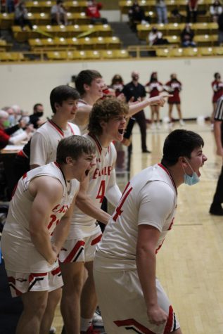The basketball team cheers on their teammates on the sidelines.