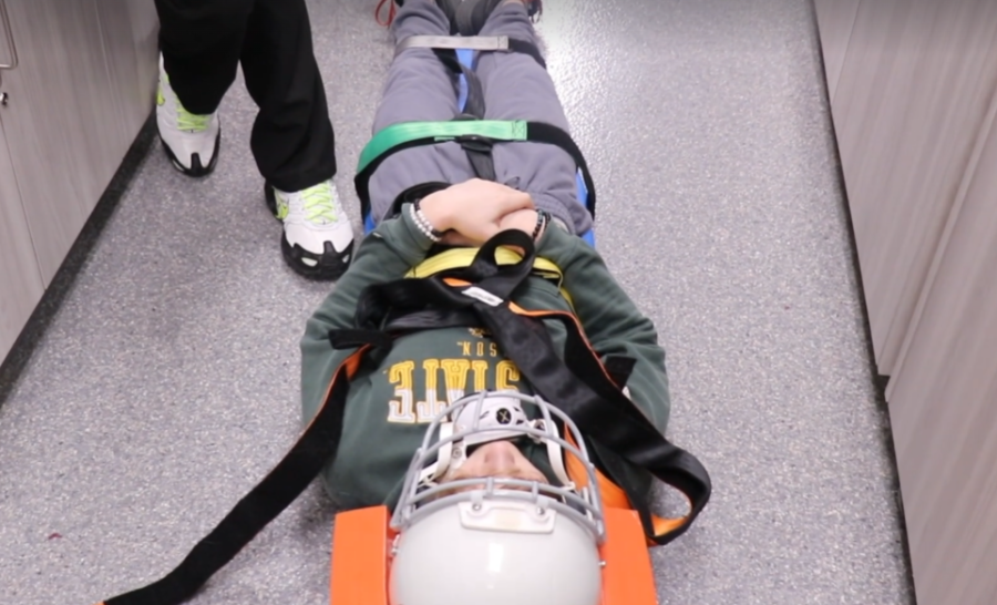 Rob Archibald places Noah Byer in a stretcher to show how athletes are pulled out of sports games when they have concussions, specifically football.