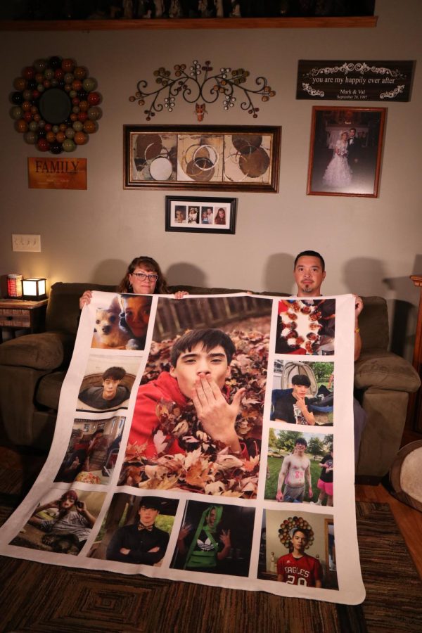 Sitting on their living room couch, Val and Mark Sandoval hold up a photo blanket containing some of their favorite photos of Isaac. 