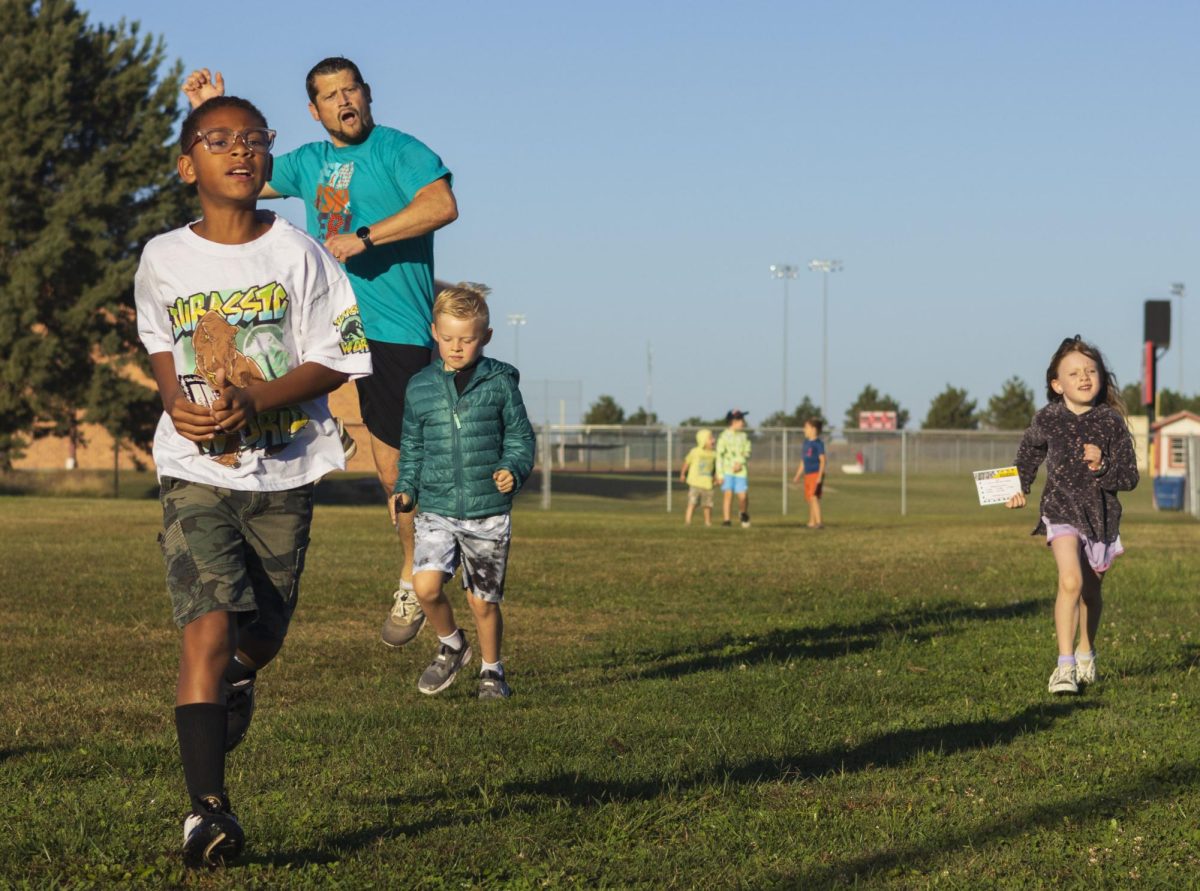 Elementary students turn the corner for their final lap cheered on by a volunteer.